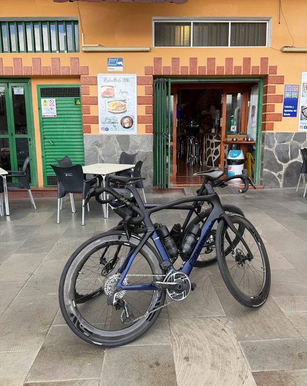 Two road bikes leaning against each other on the terrace in front of the open door, under the brown sign