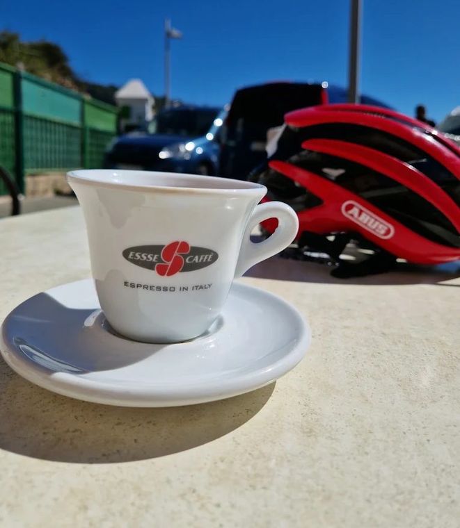 An espresso on the terrace table next to a red cycling helmet, blue sky behind